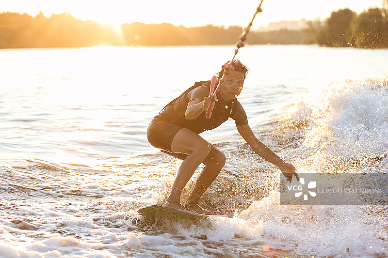 年轻自信的美丽女子在阳光明媚的夏日里在船后进行尾浪冲浪训练图片素材