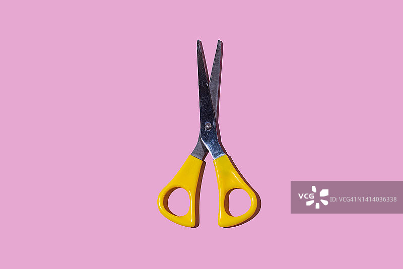 粉色背景上带有黄色手柄的金属剪刀：学校、创意概念图片素材