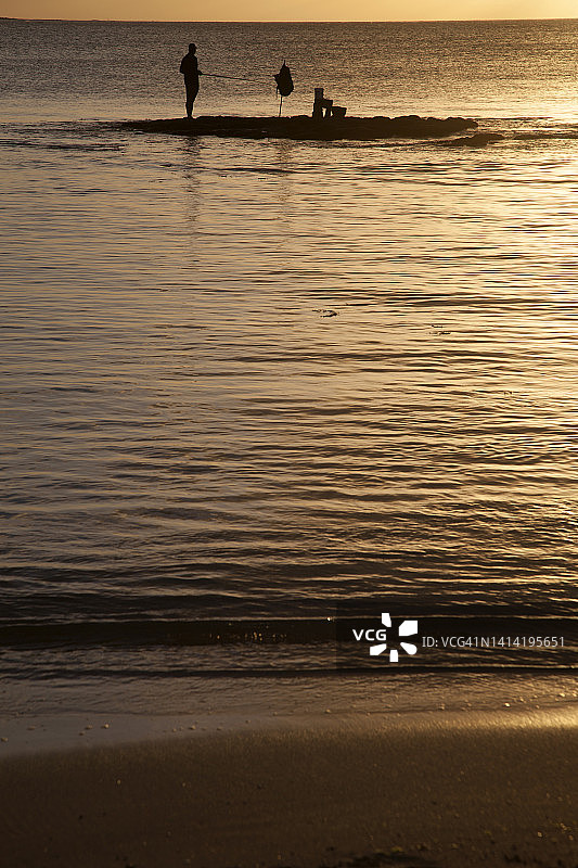 日落时分站在毛里求斯海边岩石上的渔夫剪影图片素材