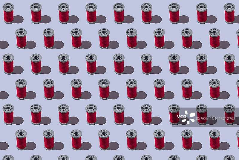 蓝灰色背景上的红色工业缝纫线轴图案：设计、纺织、缝纫、定制、服装和刺绣概念图片素材
