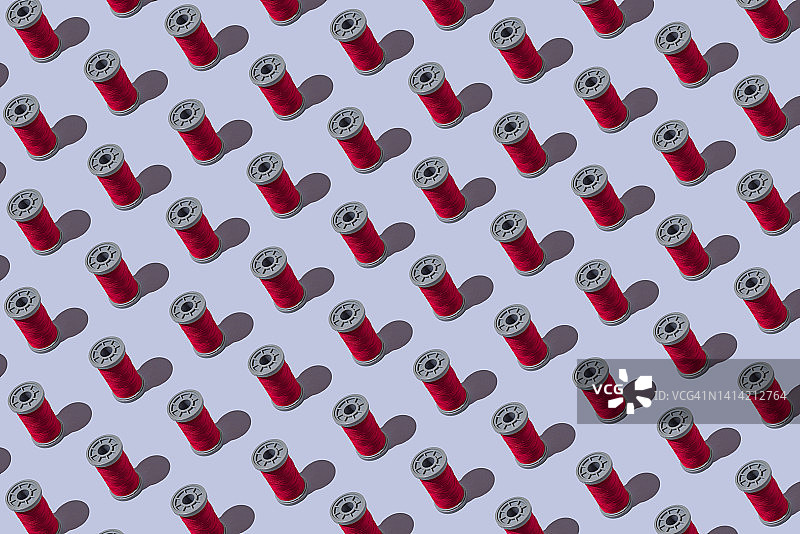 蓝灰色背景上的红色工业缝纫线轴图案：设计、纺织、缝纫、定制、服装和刺绣概念图片素材