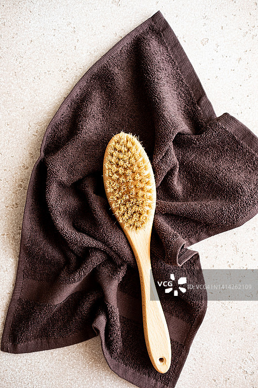 用于干刷按摩的木制身体刷和混凝土背景上的浴巾，俯视图。家庭水疗概念。零浪费。平放。复制空间。图片素材