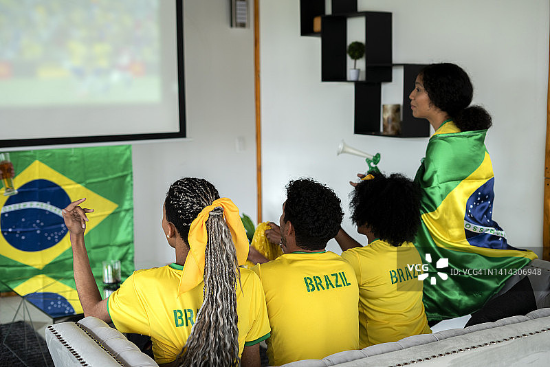 巴西队球迷身穿球衣，手持国旗，在家中全神贯注观看比赛图片素材