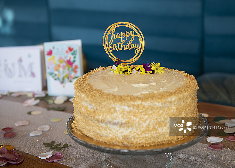生日蛋糕，配奶油糖霜和糖屑，桌上有生日贺卡和花瓣装饰图片素材