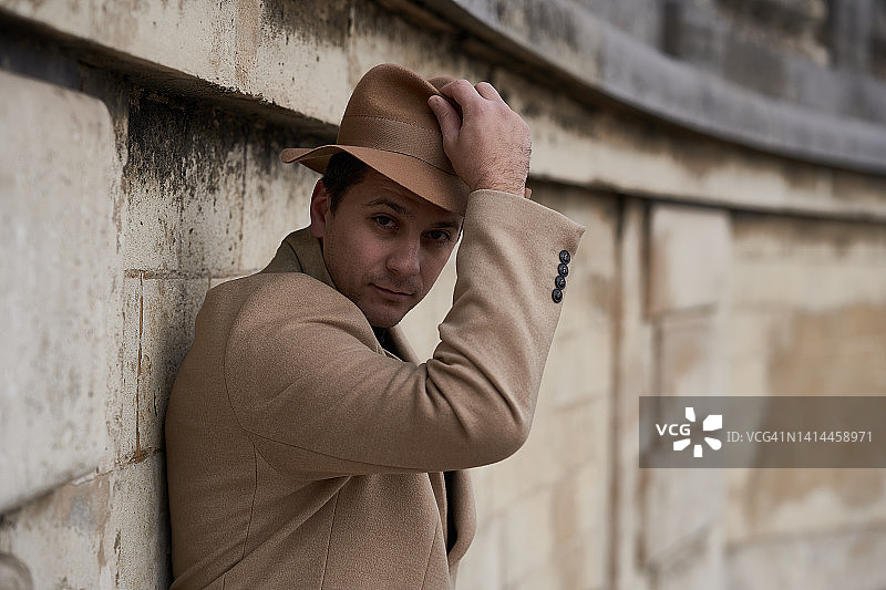 戴着米色帽子、穿着外套和黑色高领毛衣的黑发帅气男子看着镜头。40年代巴黎公园漫步男子的历史重建图片素材