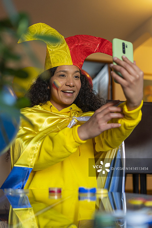 身穿厄瓜多尔足球队球衣、头戴国旗帽子的拉丁裔女人在客厅用手机自拍图片素材