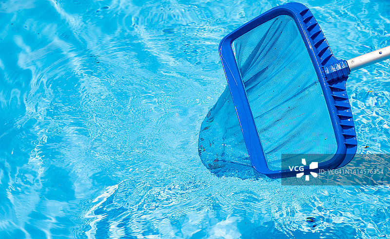 有人用长撇渣器清除漂浮在水池表面的落叶和碎屑。图片素材