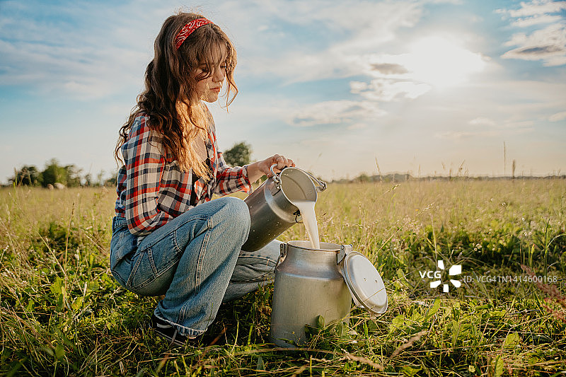 年轻女人蹲在田里将生牛奶倒入容器中图片素材