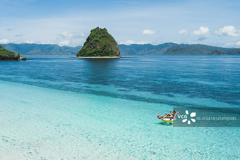 女人在热带海滩的充气独角兽上放松，可欣赏清澈的碧绿海水和山景图片素材