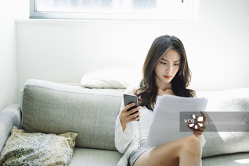 年轻亚裔女性在家使用智能手机支付账单图片素材