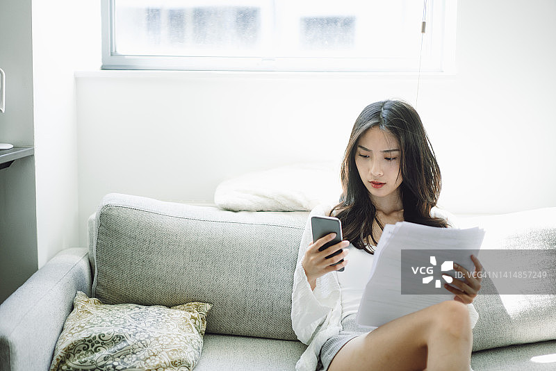 年轻亚裔女性在家使用智能手机支付账单图片素材