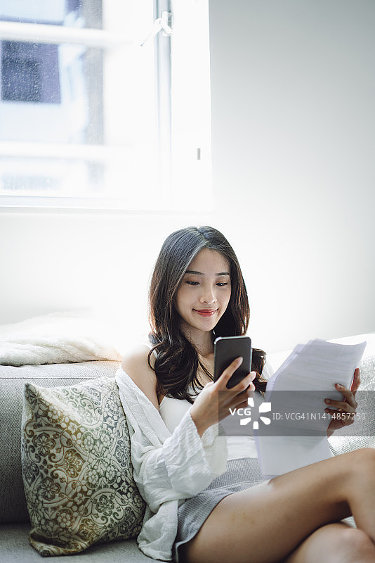 年轻亚裔女性在家使用智能手机支付账单图片素材