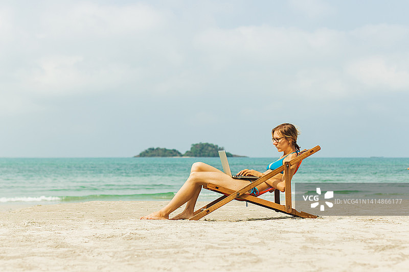 年轻商务女性在热带海滩上享受用笔记本电脑进行自由远程工作。远程工作概念。图片素材