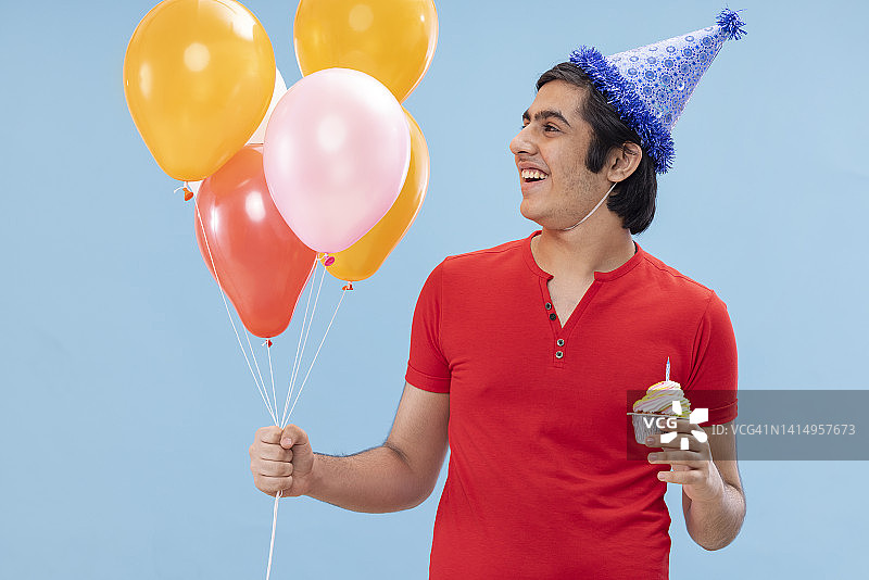 戴生日帽的快乐男孩手捧气球和蛋糕的肖像图片素材