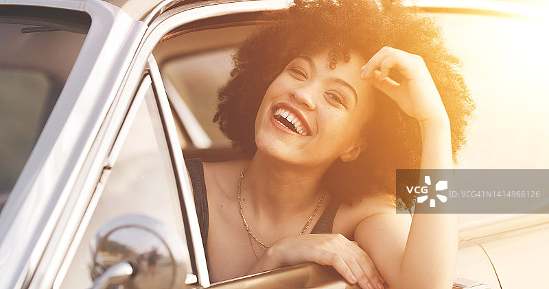 在夏季公路旅行中享受自由的微笑、无忧无虑的迷人女性。可爱的非洲裔年轻女人从打开的车窗探出头图片素材