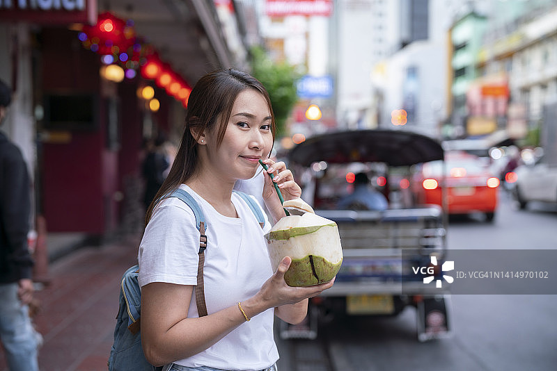 曼谷的正宗泰国街头美食：年轻女子享用美味的椰子汁图片素材