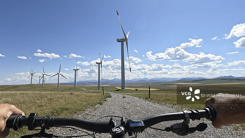 骑电动自行车驶向一排风力涡轮机的视角图片素材