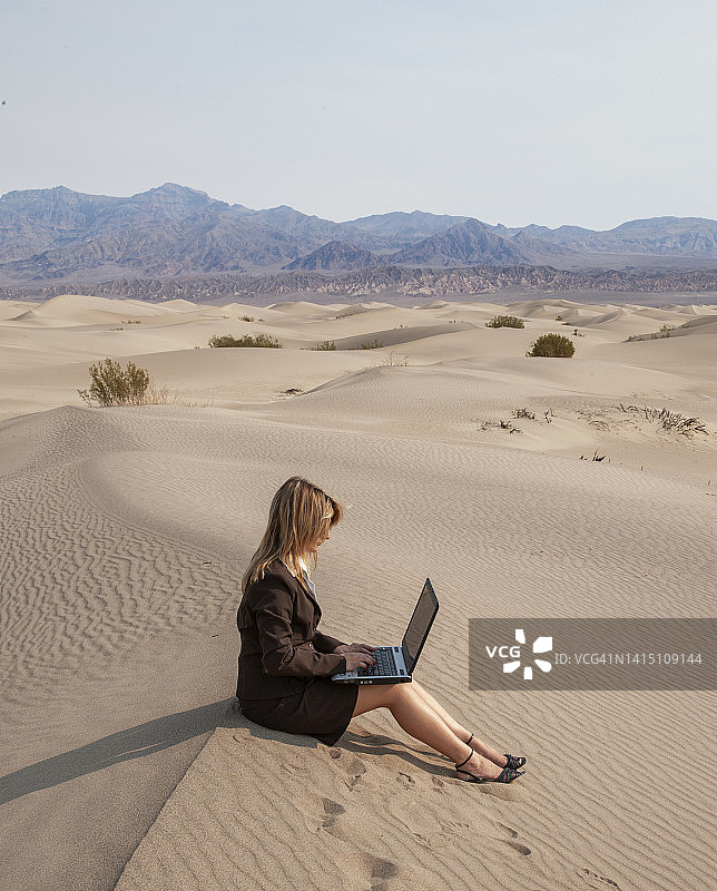 在沙丘上使用笔记本电脑的商务女性图片素材