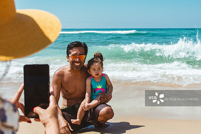 母亲在海滩给父女拍照的背影图片素材