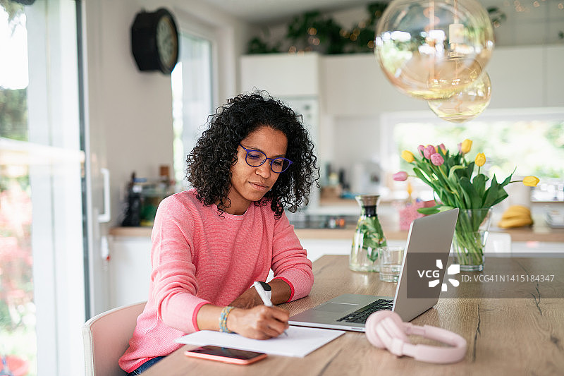 在厨房家庭办公室写笔记的混血女人图片素材