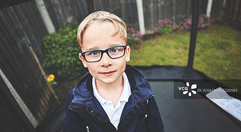 独自站在蹦床上，戴着眼镜，好奇友好的可爱书呆子小男孩肖像图片素材
