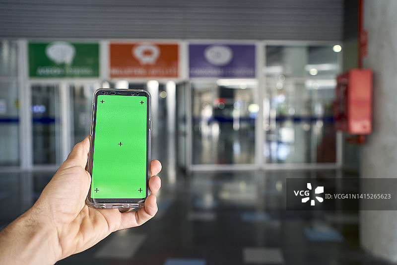 一个人在玻璃门前拿着带绿屏的手机图片素材