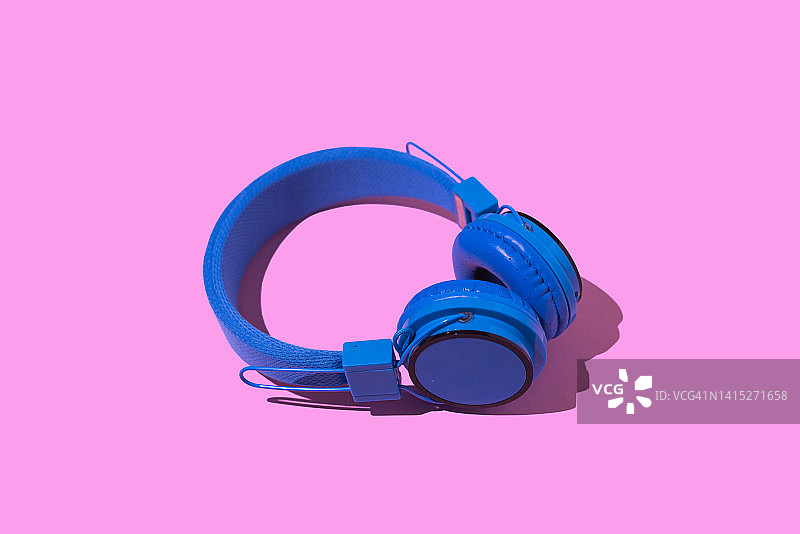 粉色背景上带有硬阴影的蓝色无线耳机：音乐、耳机、广播、播客和放松活动图片素材