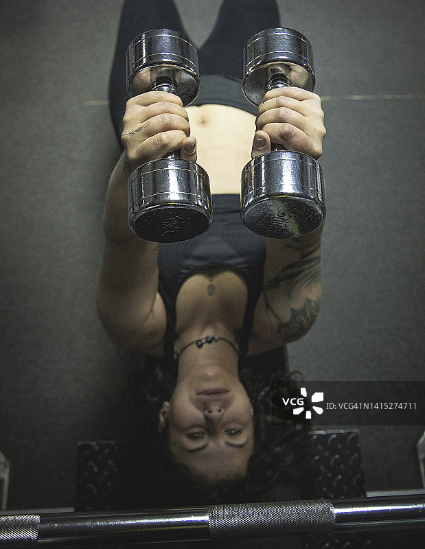 身体积极的女人躺在健身凳上，在健身房做举重哑铃锻炼图片素材