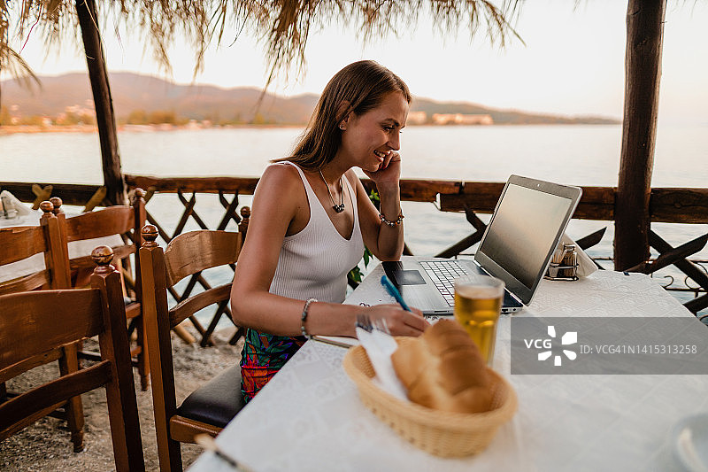 微笑的女人在度假时于餐厅使用笔记本电脑图片素材