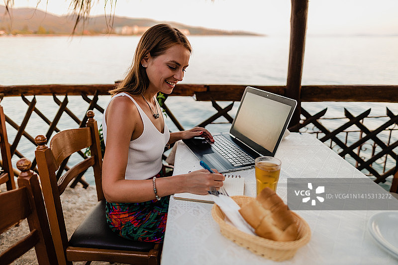 微笑的女人在度假时于餐厅使用笔记本电脑图片素材
