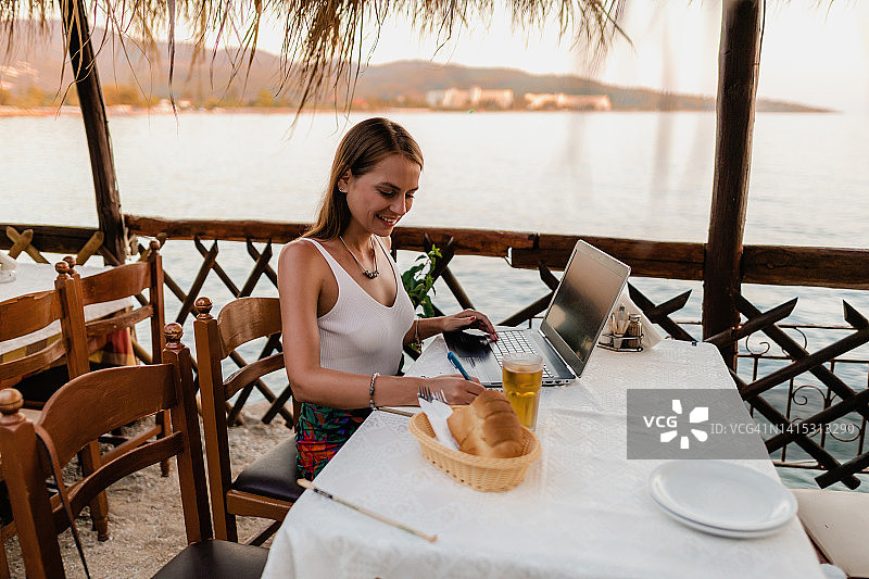 微笑的女人在度假时于餐厅使用笔记本电脑图片素材