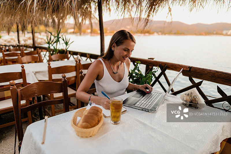 年轻女人在海边餐厅使用笔记本电脑图片素材