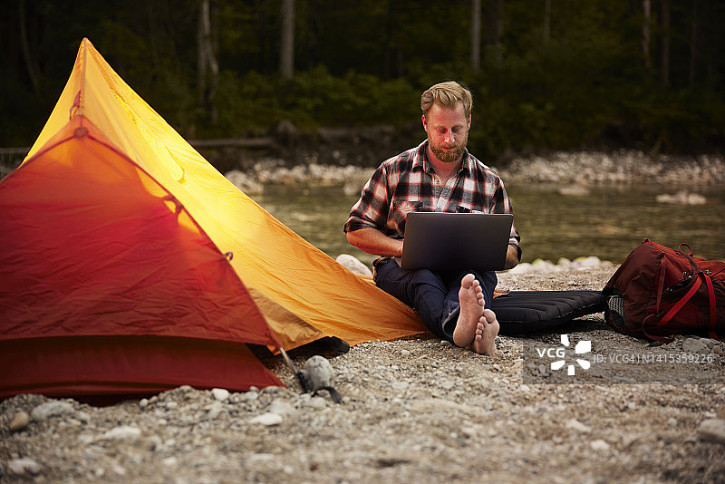 商人坐在河岸的帐篷旁使用笔记本电脑图片素材