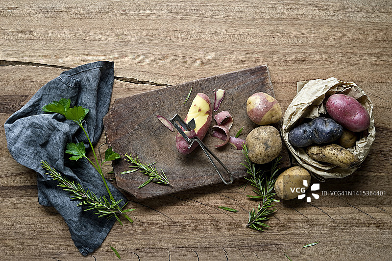 草药、餐巾、砧板、削皮器和不同品种的生土豆图片素材