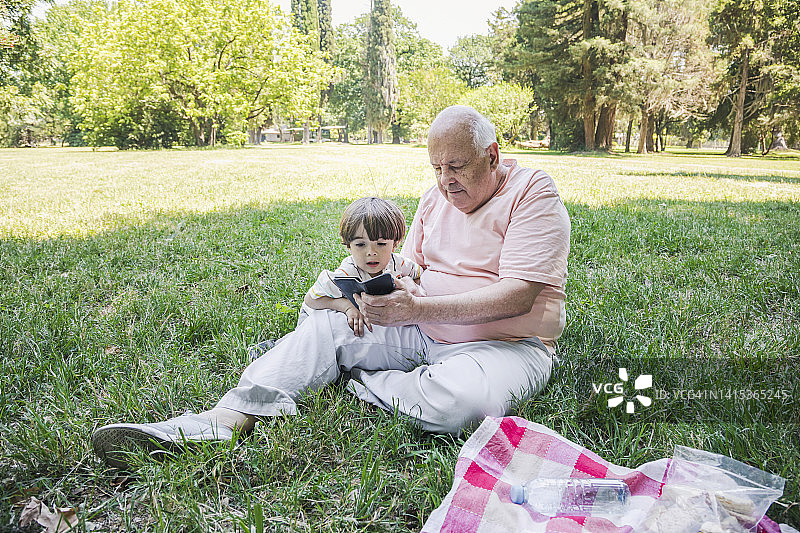 男孩和爷爷在公园使用智能手机图片素材