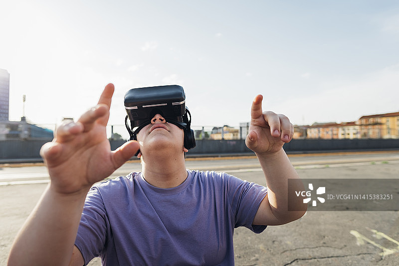 青少年男孩在人行道上佩戴VR模拟器并做手势图片素材