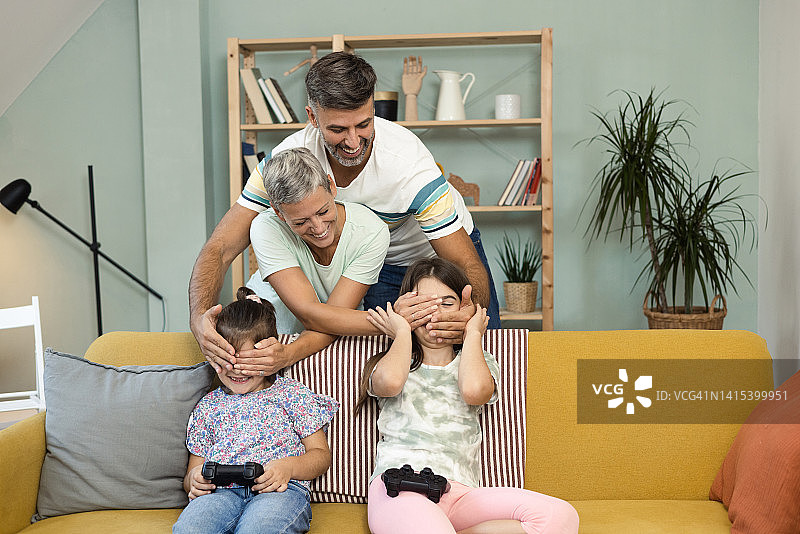 父母在两个女儿玩游戏时捂住她们的眼睛图片素材