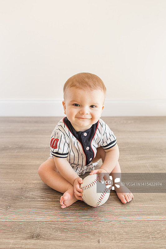 7个月大的男婴穿着棒球服，在地板上玩垒球图片素材