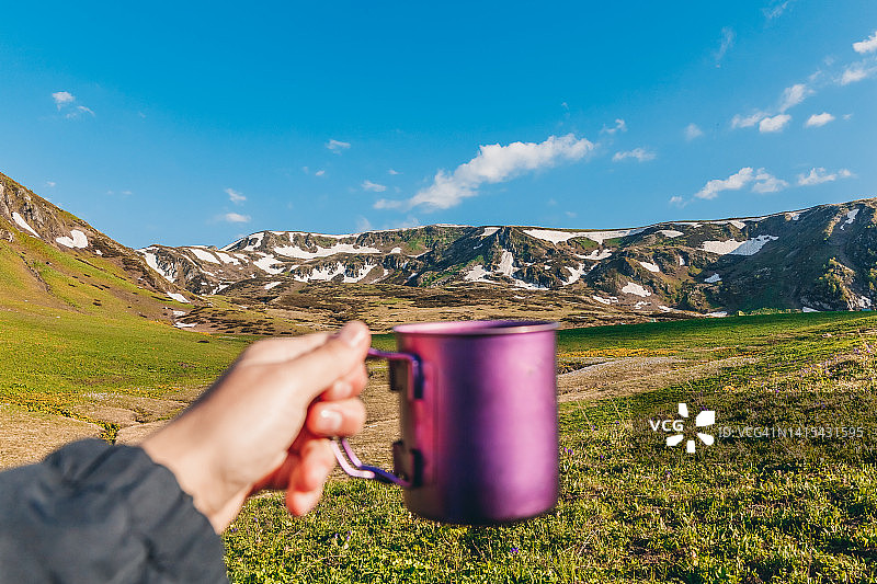 在山地背景下手持露营杯的人手POV图片素材