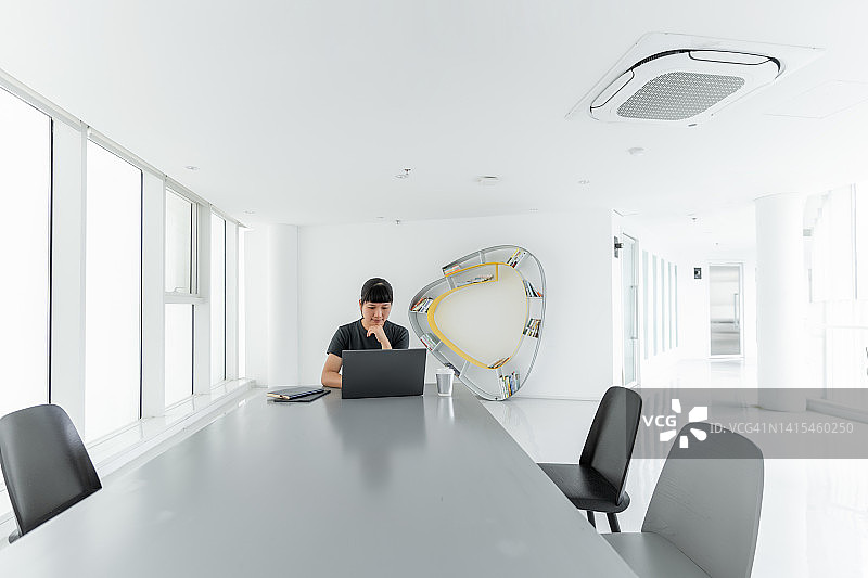 一位亚洲女性在宽敞、简洁、明亮的会议室里用电脑进行在线学习图片素材