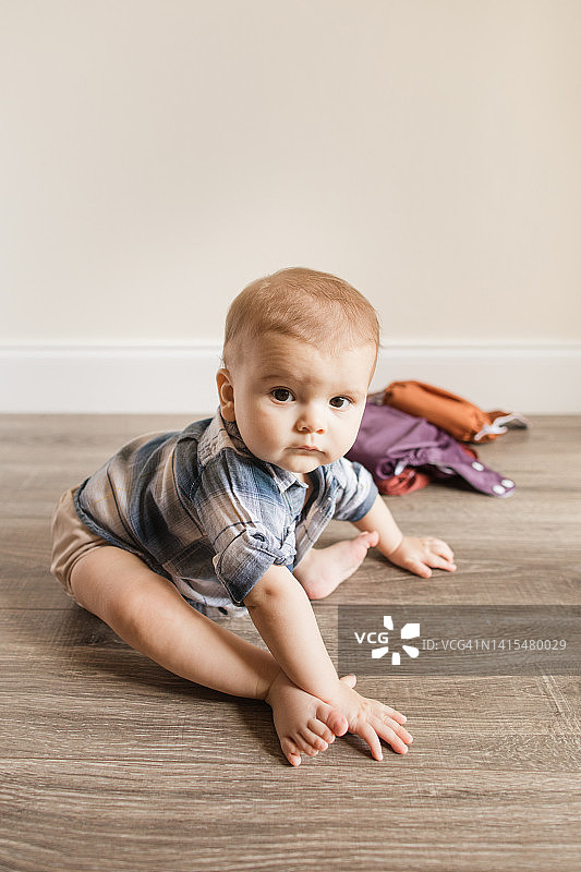 患有多指症的7个月大男婴学习坐立的新技能，穿着中性色可重复使用的尿布图片素材
