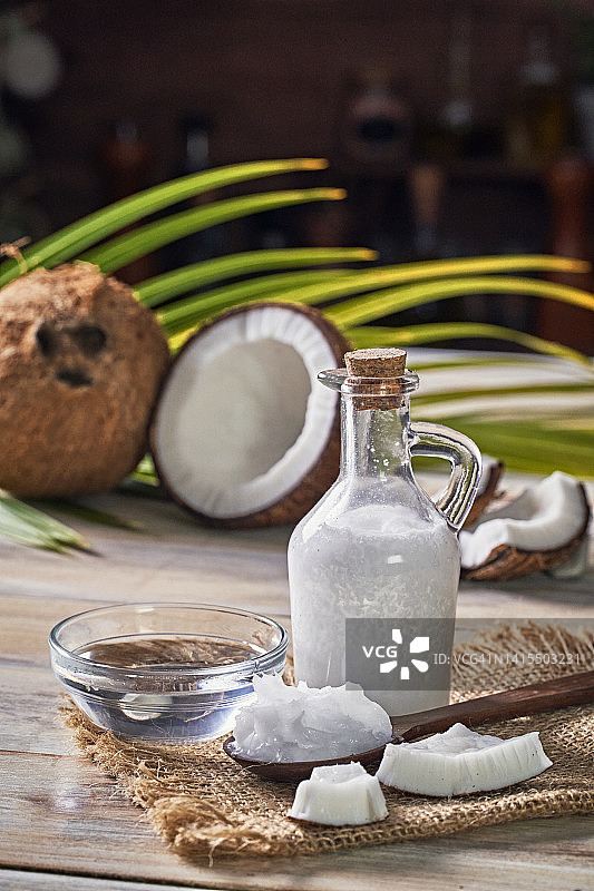 木质背景上的椰子油玻璃瓶和新鲜椰子图片素材