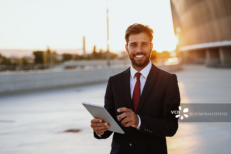 现代街区使用平板电脑的西装革履的年轻男商人或金融专家，看着镜头图片素材