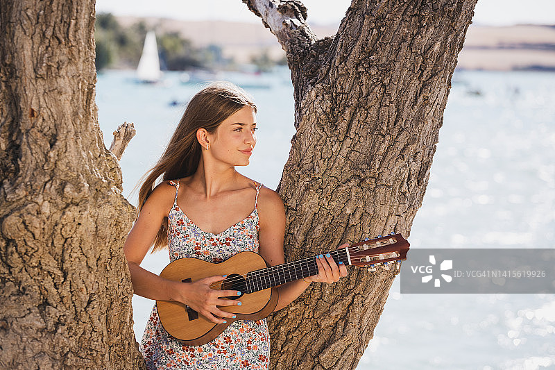 年轻漂亮的女孩在户外湖面上弹吉他图片素材