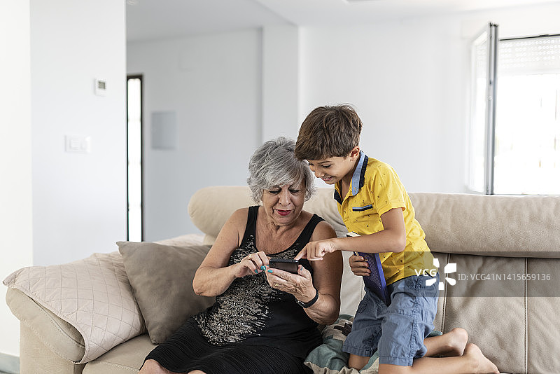 祖母和孙子在家里的沙发上一起玩手机图片素材
