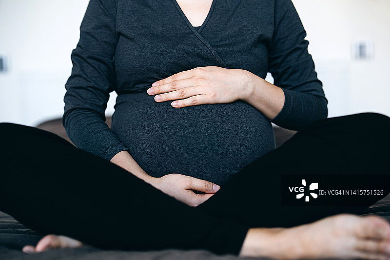 亚洲孕妇坐在床上轻抚孕肚图片素材