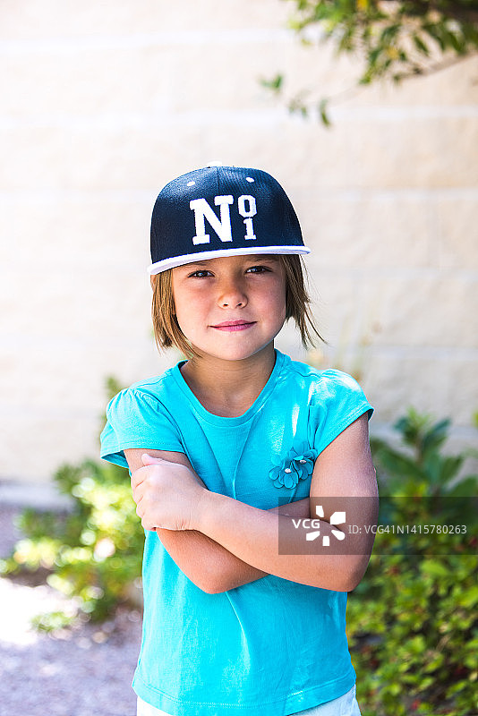 戴黑白棒球帽的绿衣金发女孩：第一名，微笑，双臂交叉。童年，肖像，漂亮，可爱，情感概念图片素材