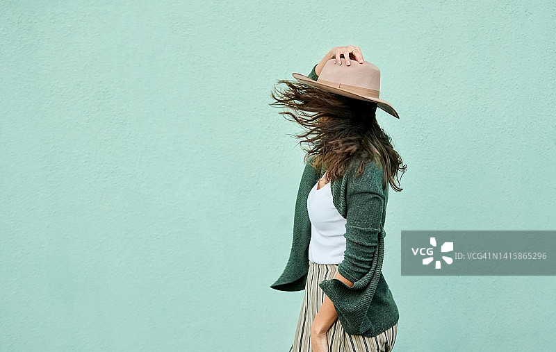 年轻女子在微风中拿着帽子的侧视图图片素材