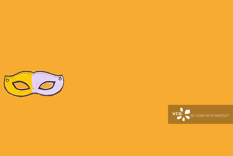 儿童在黄色背景上绘制的庆祝狂欢节的黄白色纸板面具图片素材