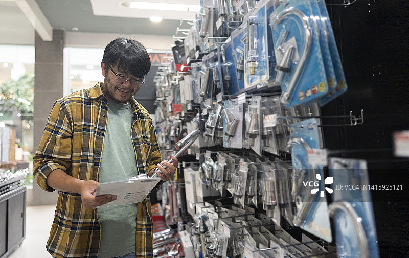 亚洲年轻人带破损水龙头去五金店更换图片素材
